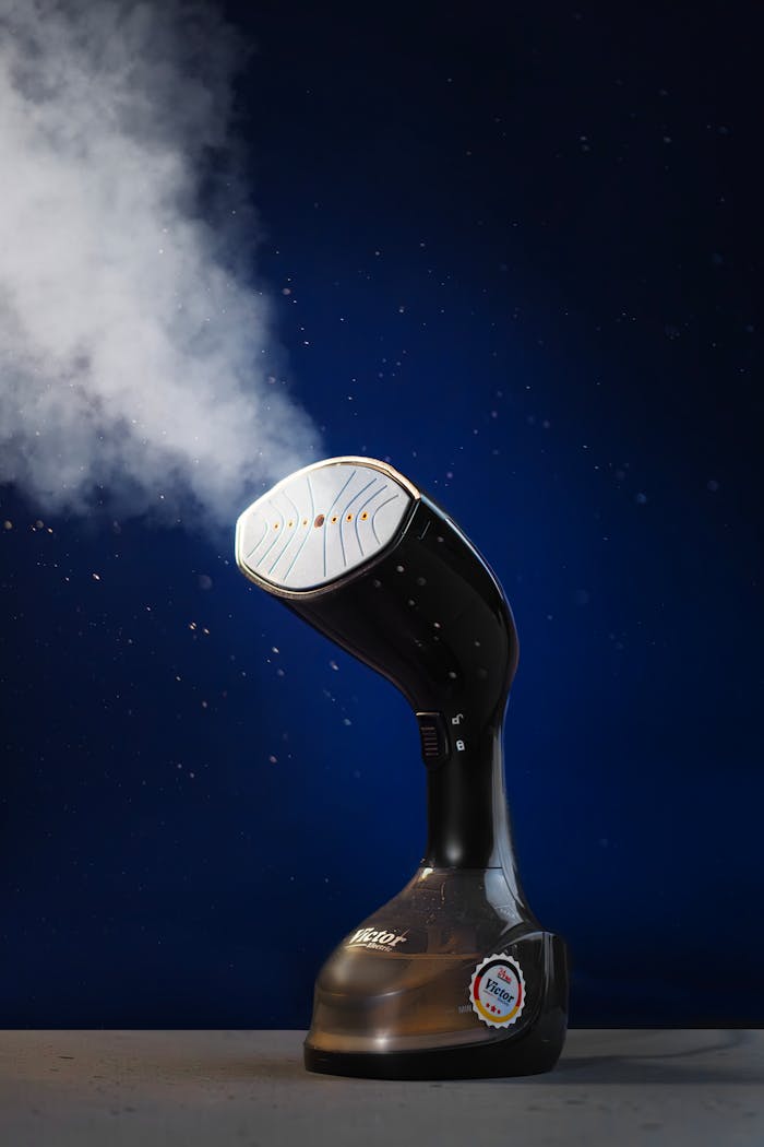 Handheld garment steamer releasing steam, isolated on dark blue background with spotlight effect.